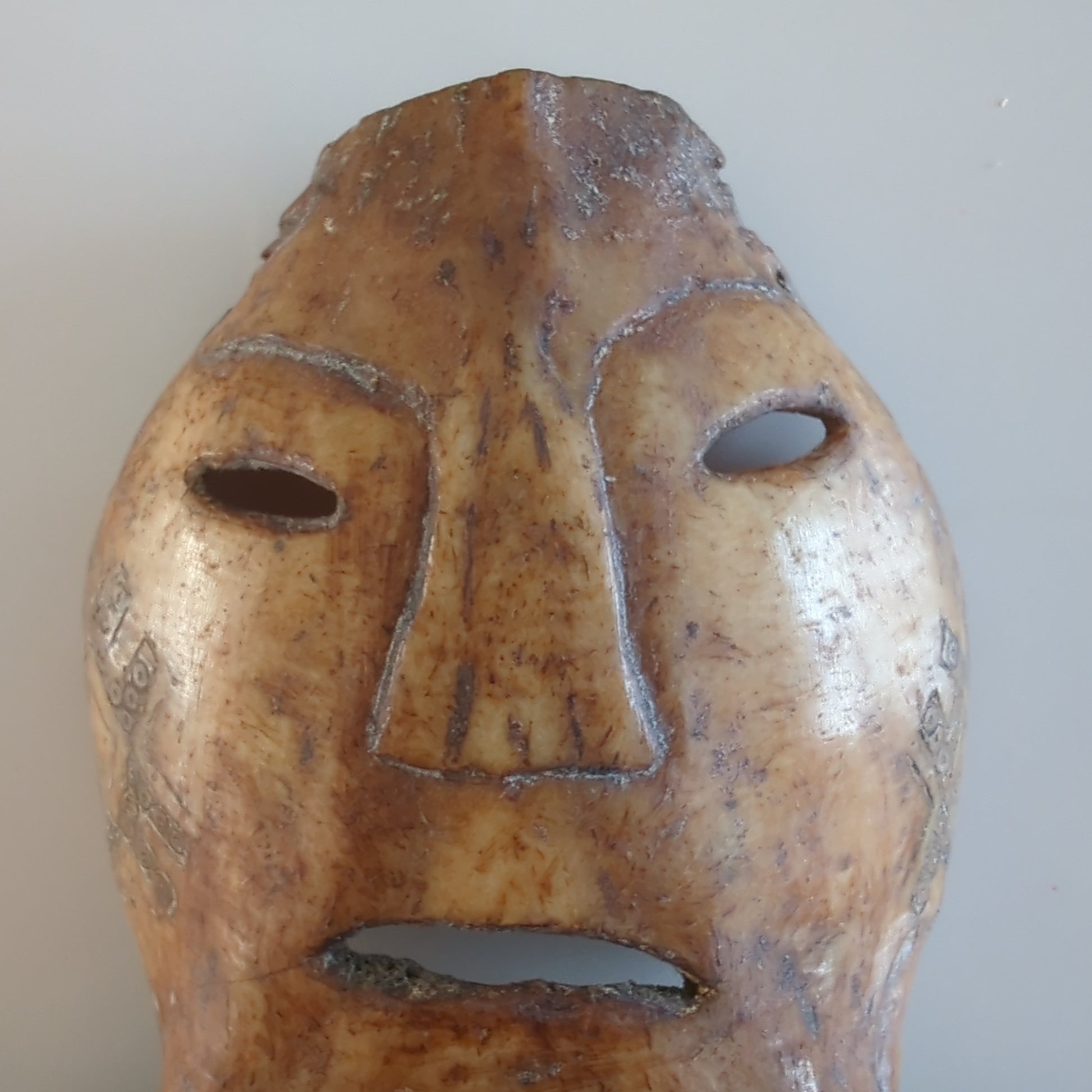 Face Close-up: A frontal close-up of the amulet's carved face, emphasizing the simple, stylized features like the nose and eyes.