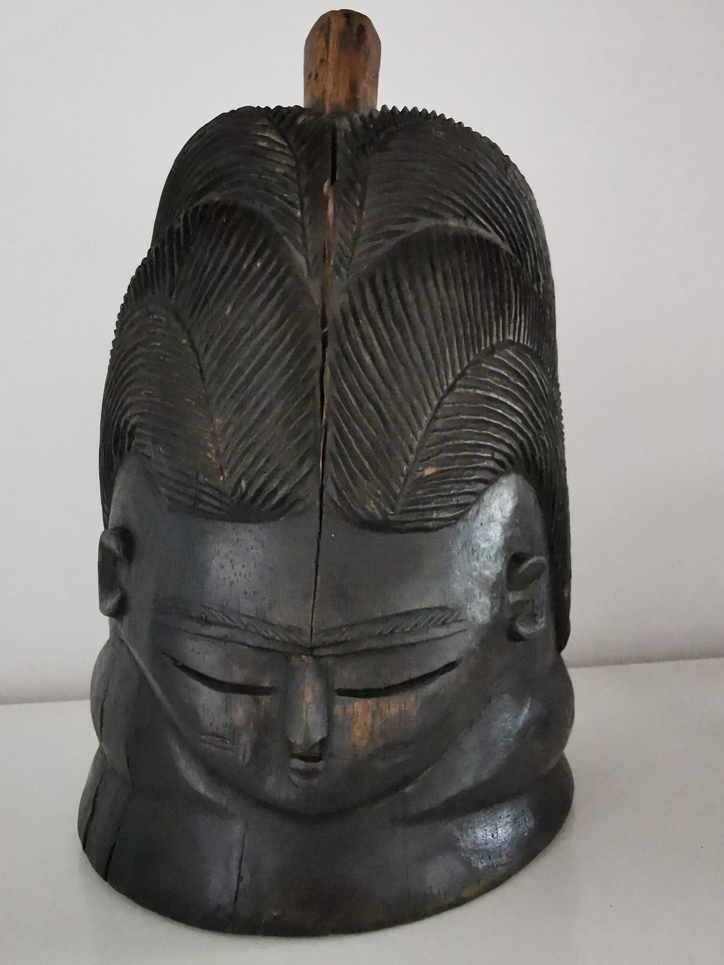 An ebonised wood Mende Sowei helmet mask with a high forehead, intricate hairdo, and neck rings.