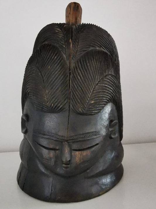 An ebonised wood Mende Sowei helmet mask with a high forehead, intricate hairdo, and neck rings.
