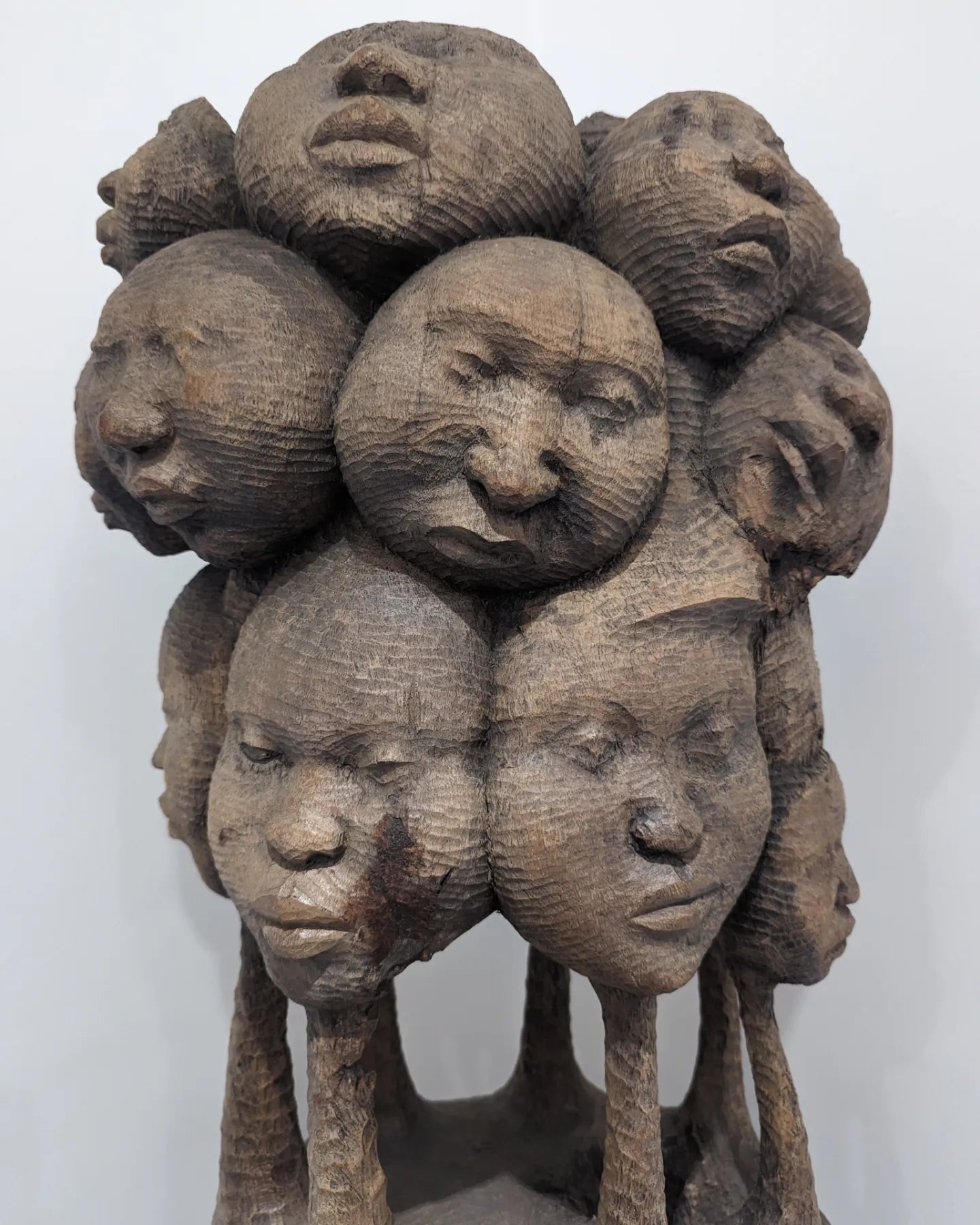 A side-profile close-up of the stack of faces at the top of the sculpture, showing their dimensional carving