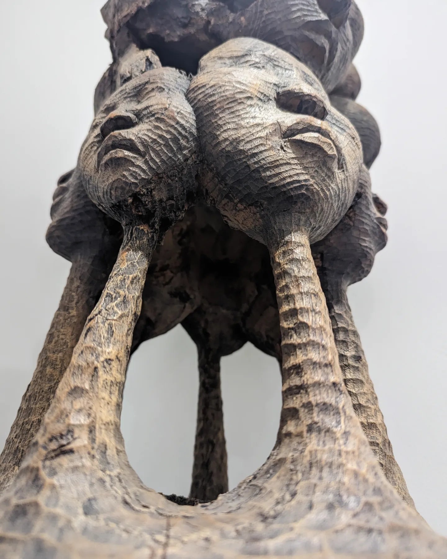 An angled, close-up shot of the top cluster of faces on the sculpture, highlighting the details of their individual expressions and features.