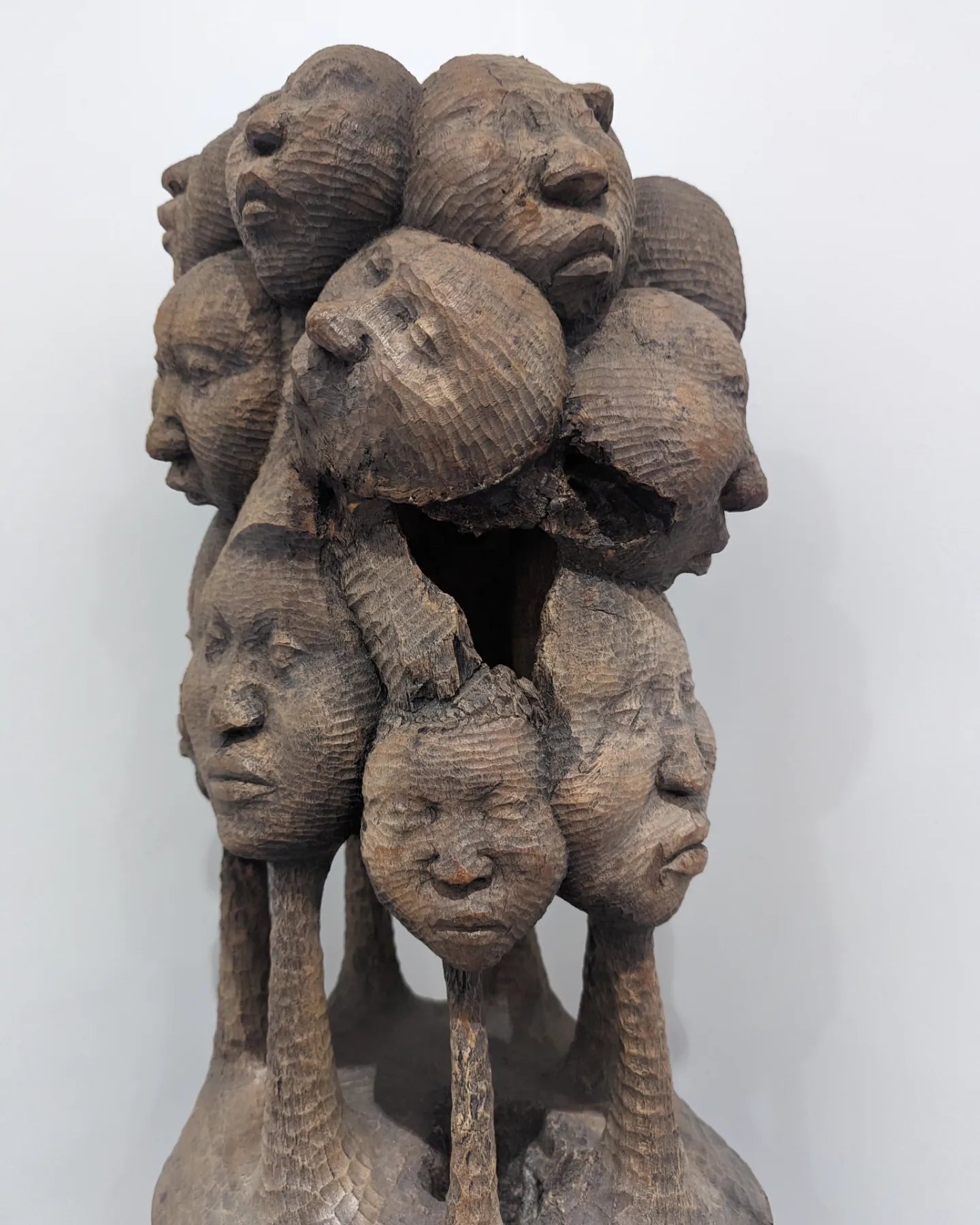 A close-up front view of the uppermost portion of the sculpture, showing a cluster of finely carved wooden faces grouped together.