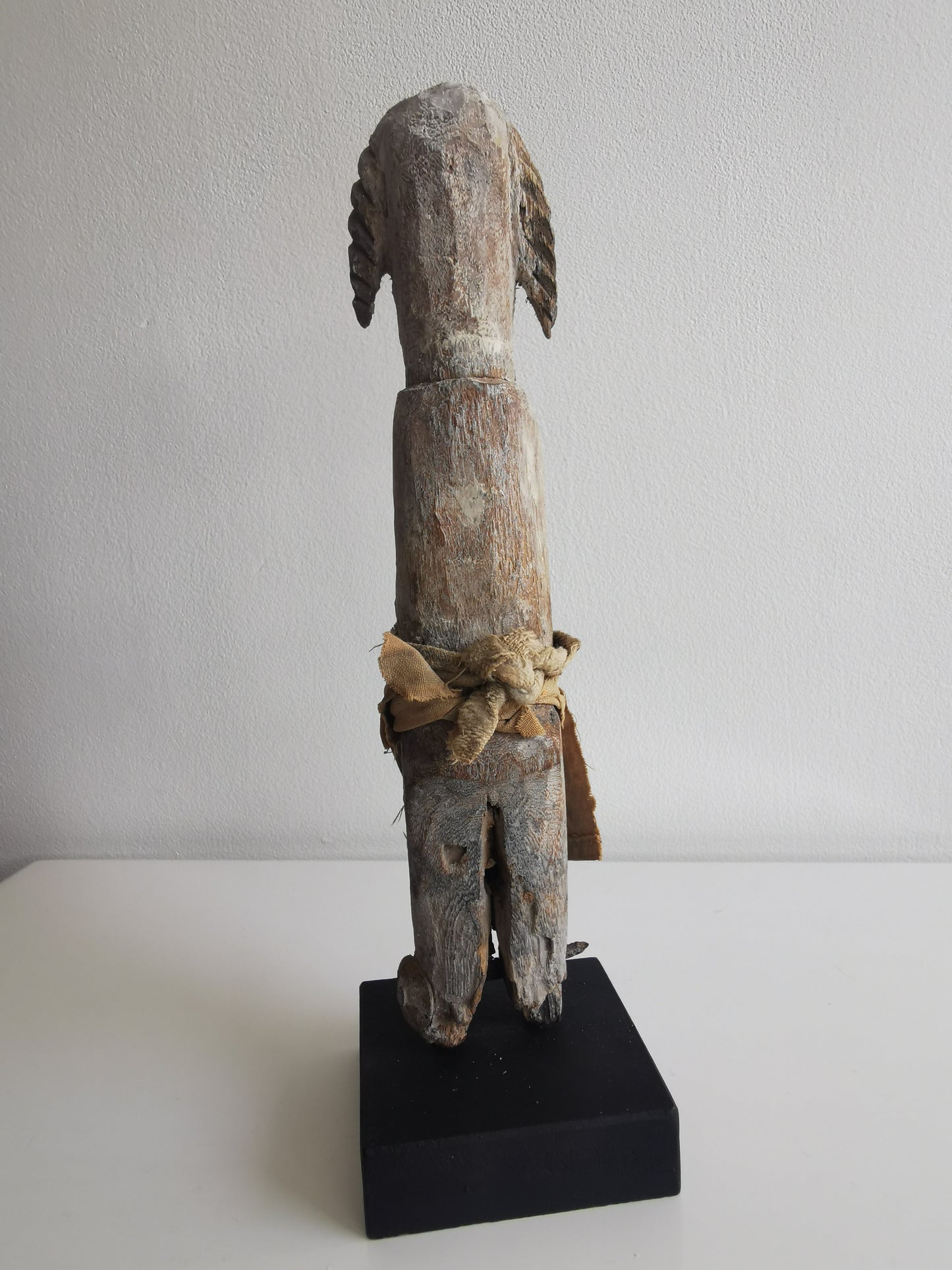 A side profile of the Ibibio statuette on its stand, revealing its slender body and the way the cloth is wrapped around the lower half of the figure.