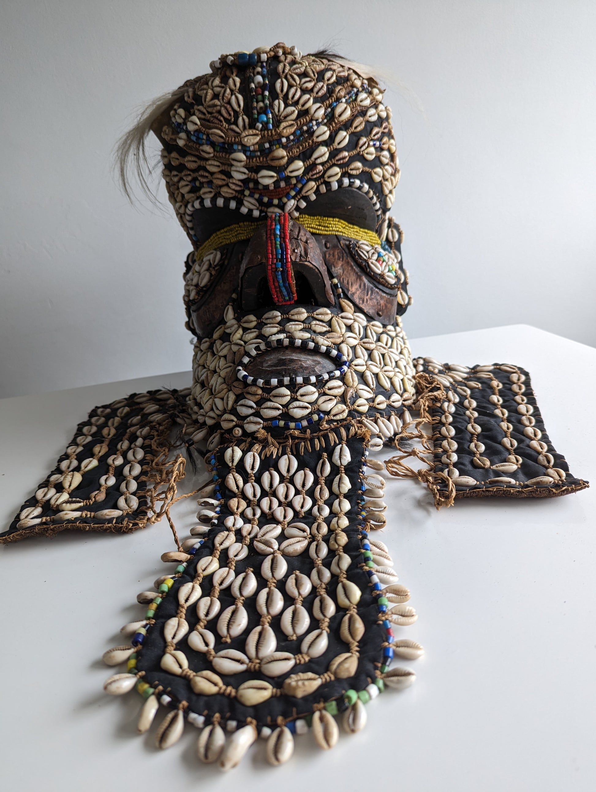 A full front view of the Kuba 'Bwoom' mask, showing the entire helmet with its elaborate shell and beadwork decorations on the face, neck, and shoulder flaps.