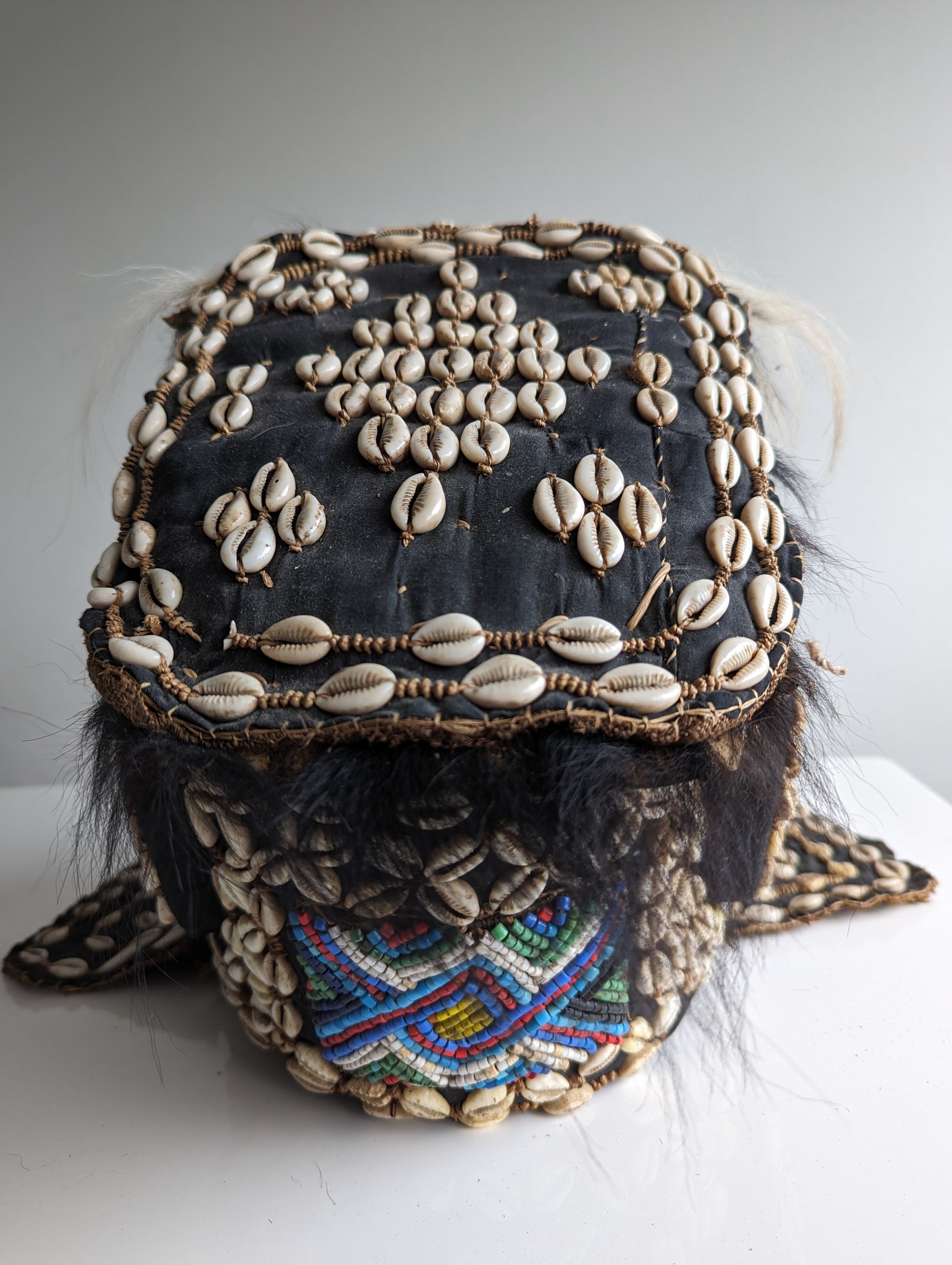 A top-down view of the Kuba helmet mask, showing the elaborate shell-covered headpiece from above and the large, open mouth