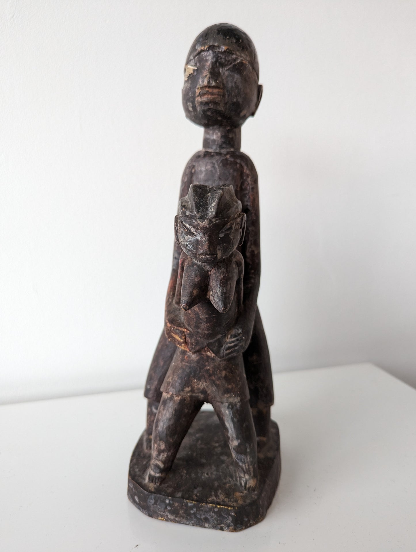 A side view of a wooden Lobi sculpture of two figures, one standing behind the other.