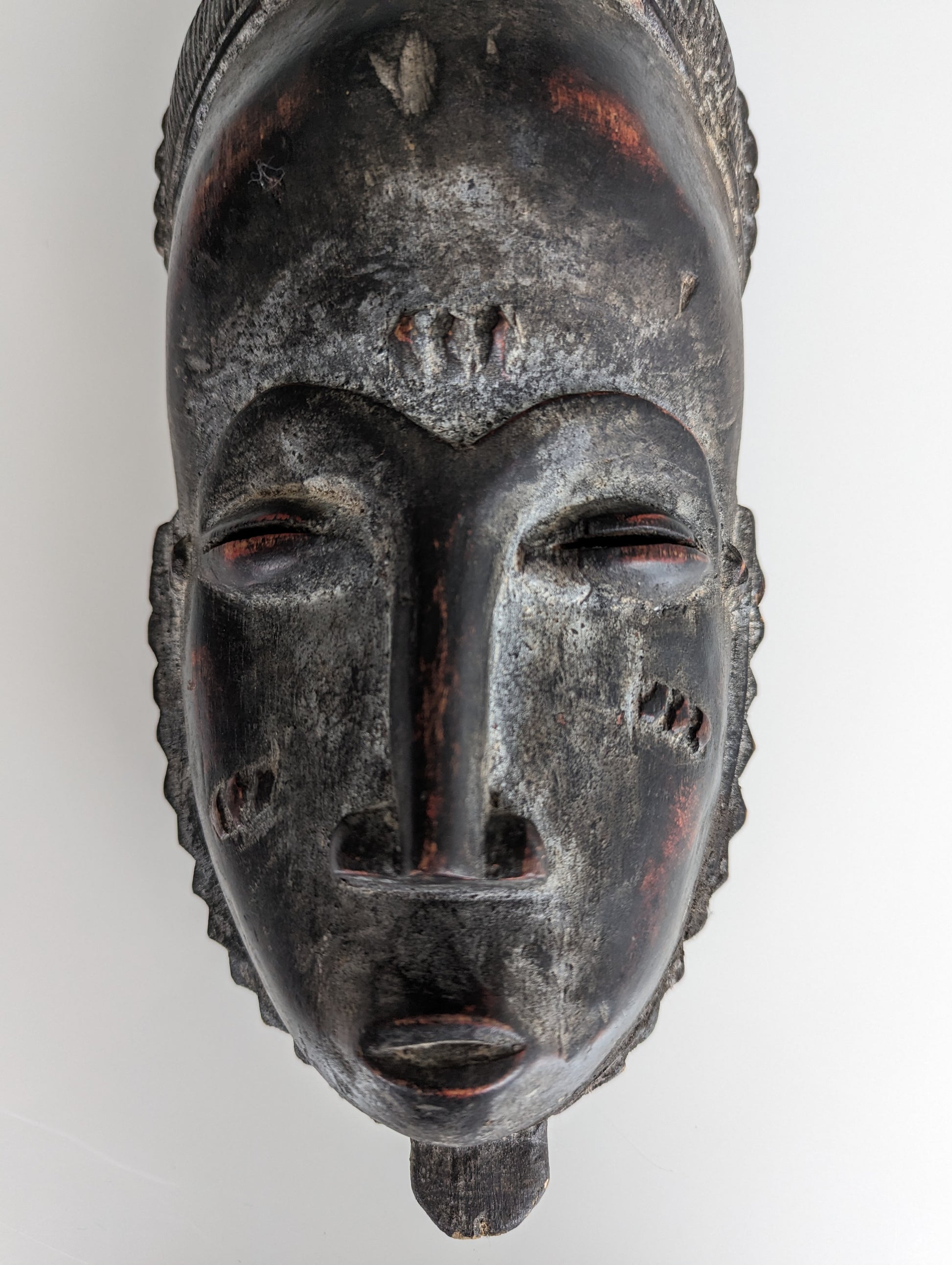 A close-up of the mask's face, highlighting the symmetrical features, fine details of the carving, and the reddish pigment used in some areas.