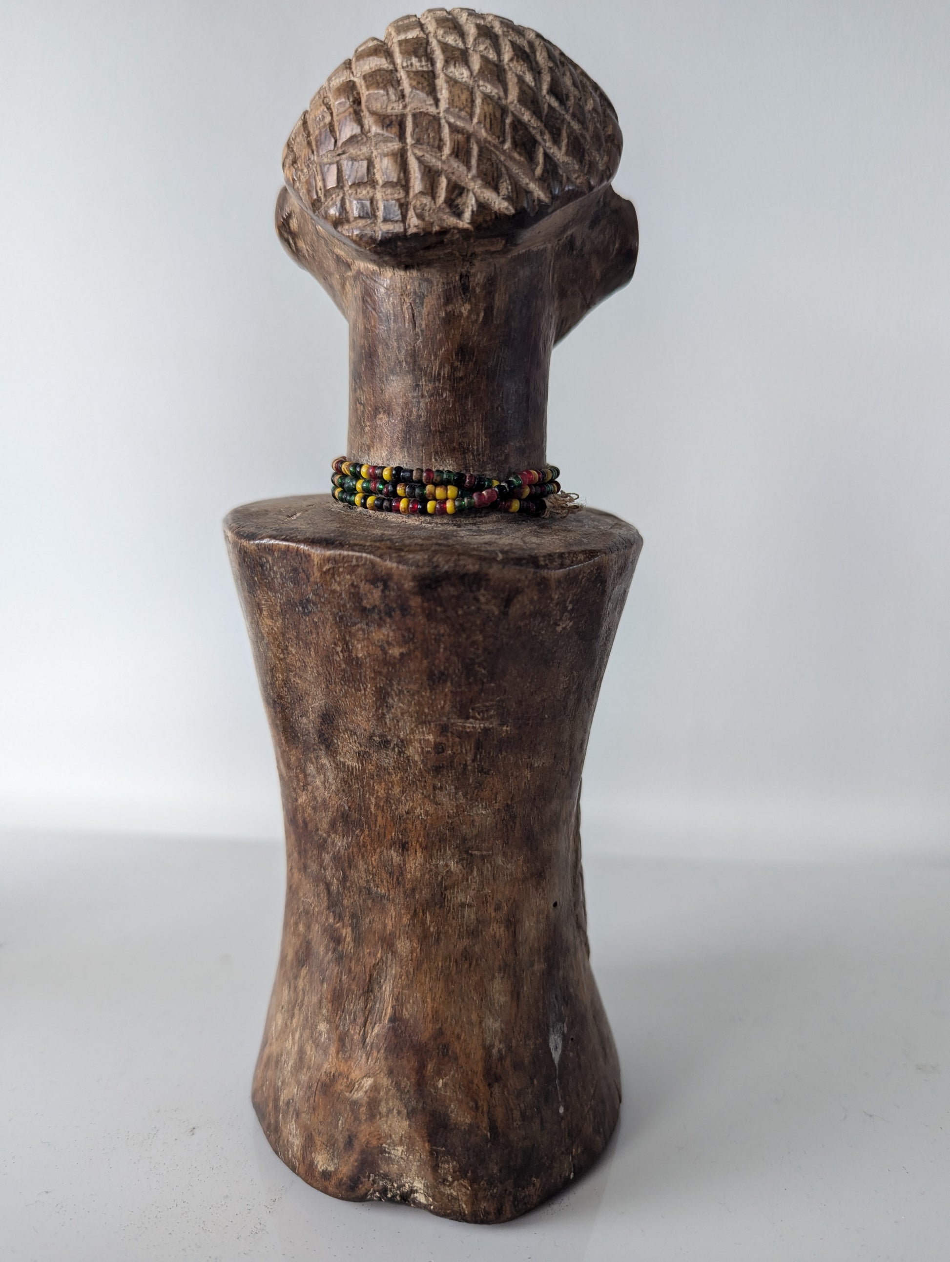 A full-body frontal view of the Tabwa Mpundu doll, showing its carved head, beaded necklace, and the textured torso with geometric patterns.