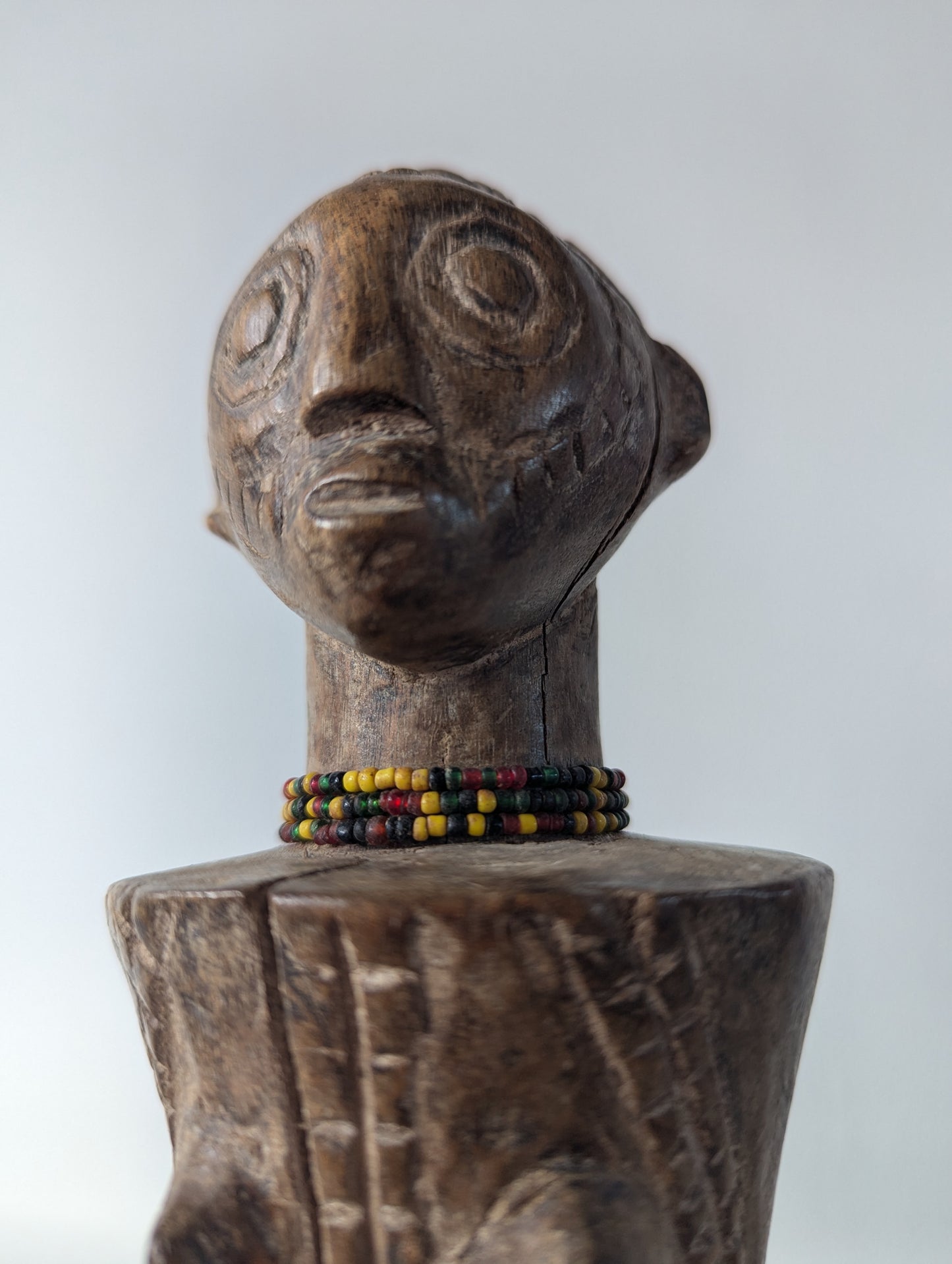 A close-up profile of the tabwa doll's head and shoulders. This angle highlights the elongated, stylized face and the small beaded necklace.