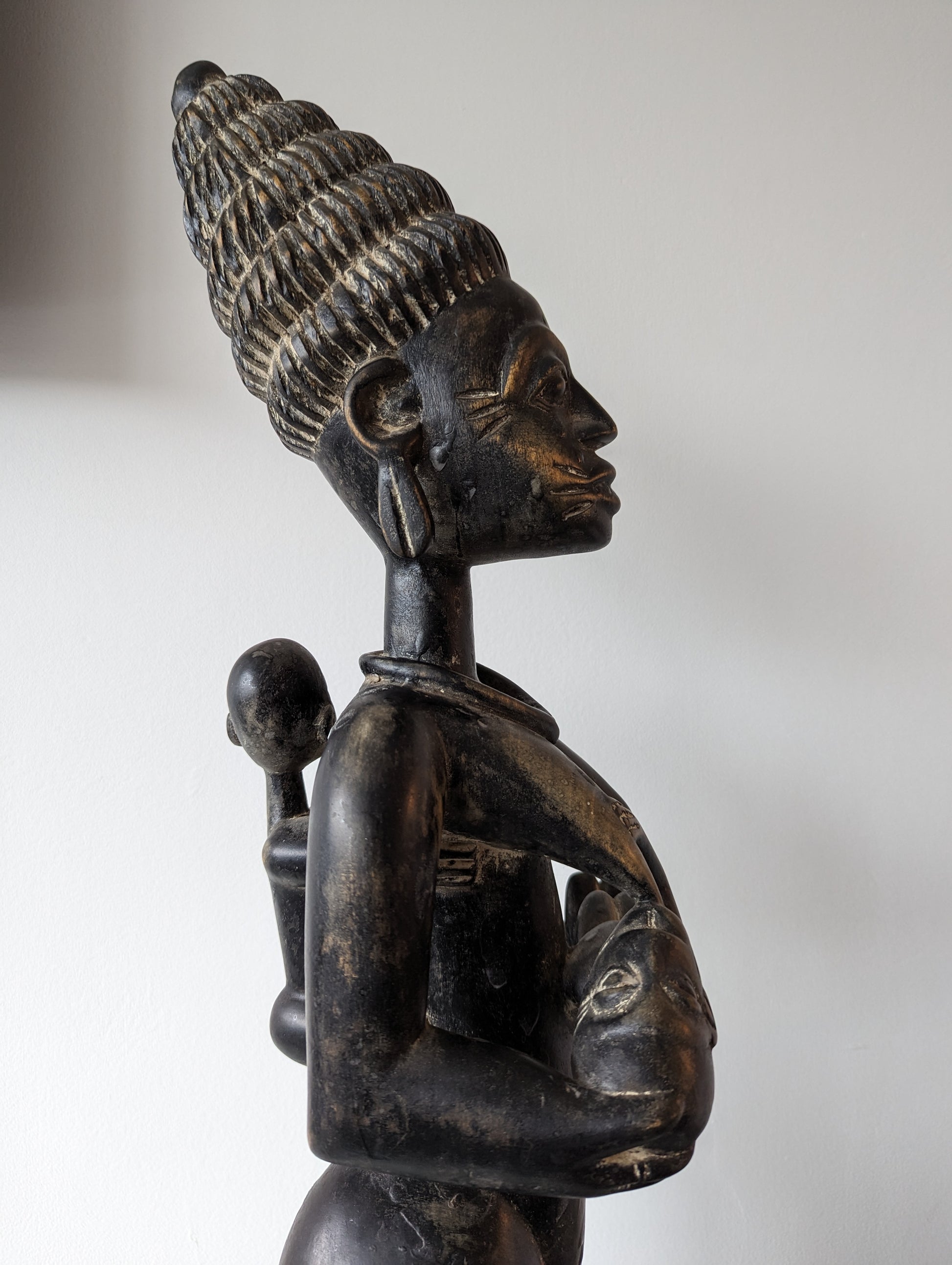 An angled view of the Yoruba statue from the side, showing the depth and three-dimensionality of the carving.