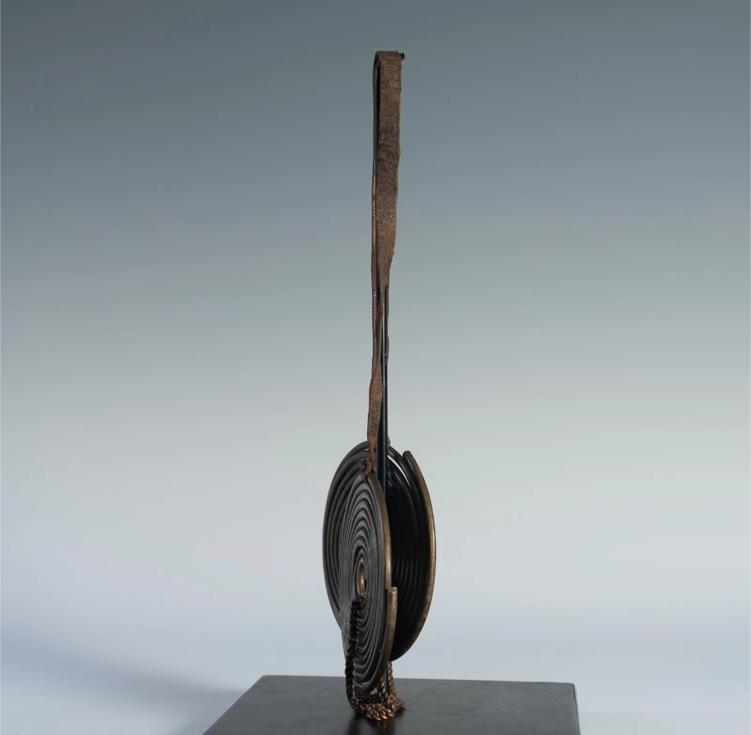 Side profile of the Maasai coiled brass neck adornment, showing its thin, flat form and the details of the coiled brass wire