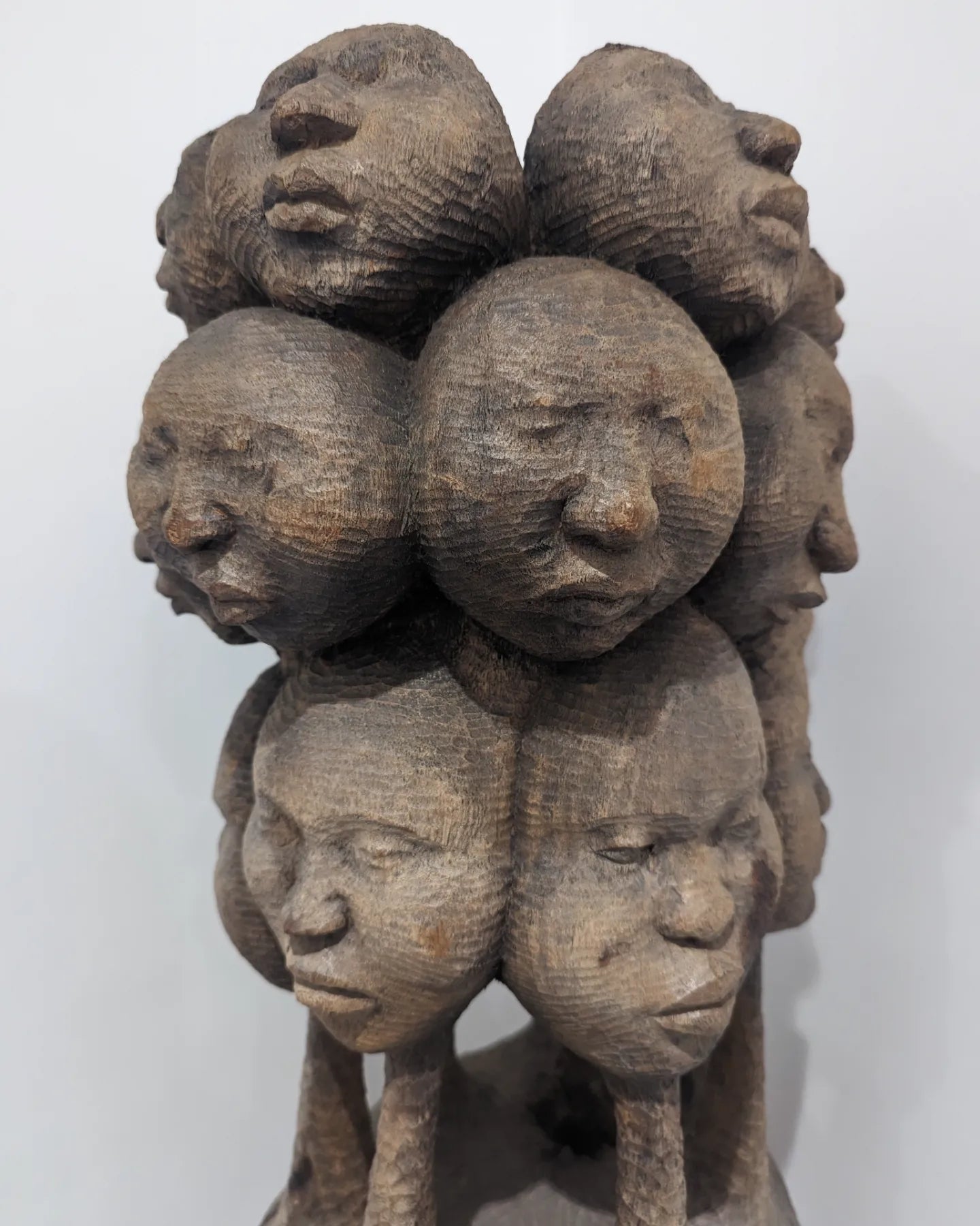 A close-up view of the lower cluster of faces on the sculpture, just above the central column.