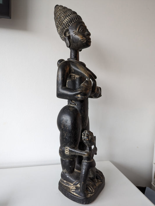 A side profile of the Yoruba statue, showing the woman's full body and the position of the baby in her arms.