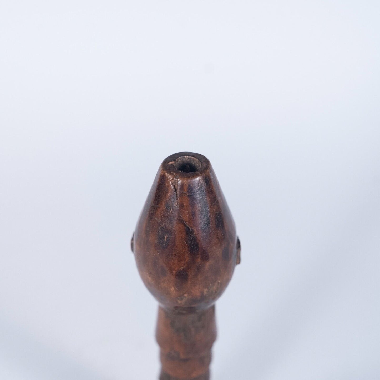 A close-up view of the top of the wooden staff handle, showing the carved face from a direct front angle.
