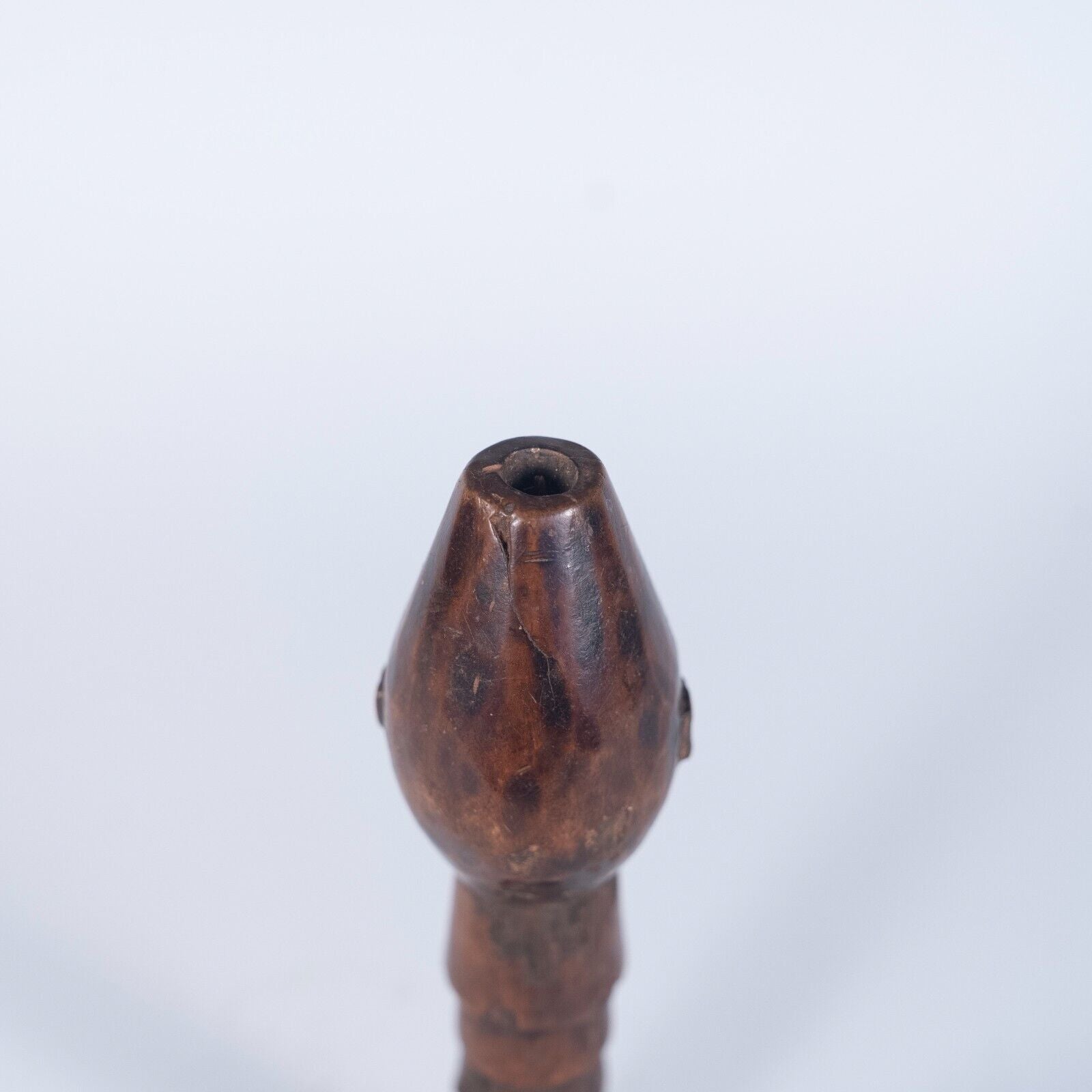 A close-up view of the top of the wooden staff handle, showing the carved face from a direct front angle.