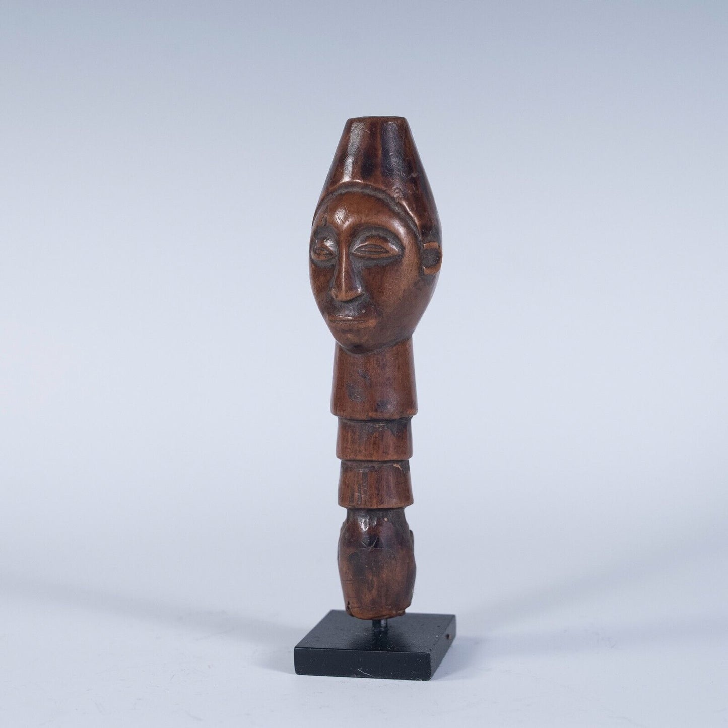 A full view of the staff handle on its stand, showing its elongated, cylindrical shape and the carved face at the top.
