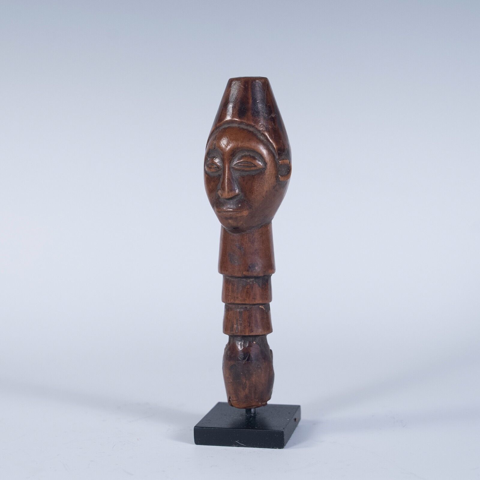 A full view of the staff handle on its stand, showing its elongated, cylindrical shape and the carved face at the top.