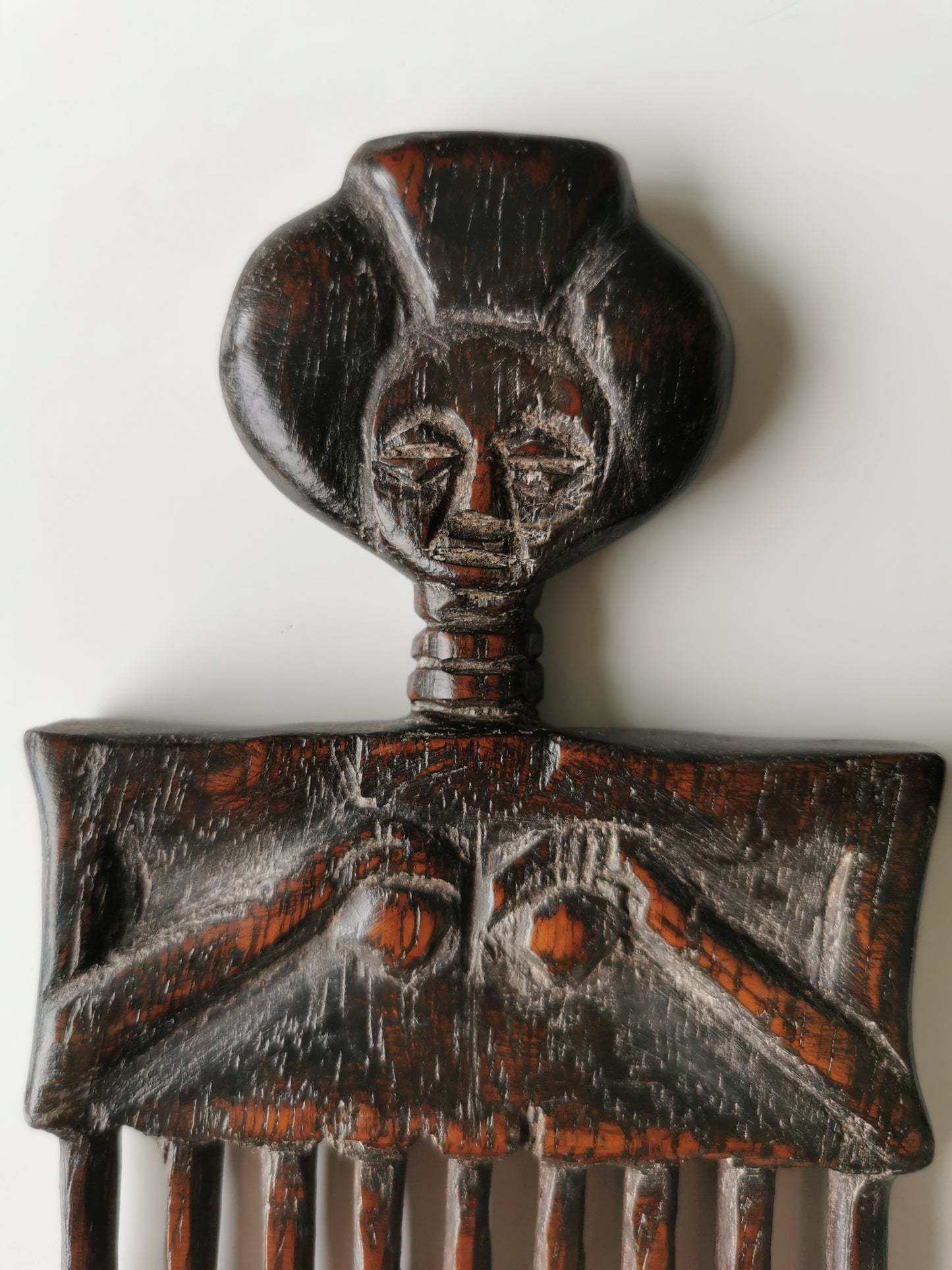 A close-up of the carved female figure on the hair comb, highlighting the details of her facial features and the hands on her torso.