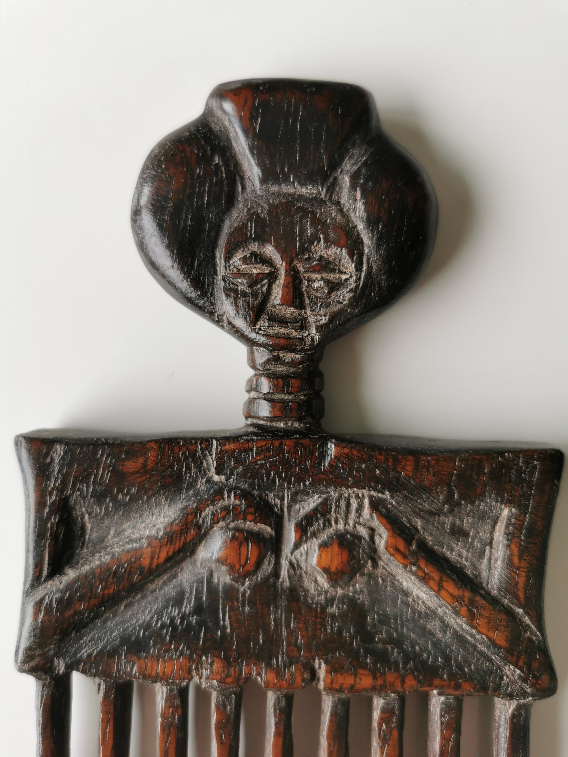 A close-up of the carved female figure on the hair comb, highlighting the details of her facial features and the hands on her torso.