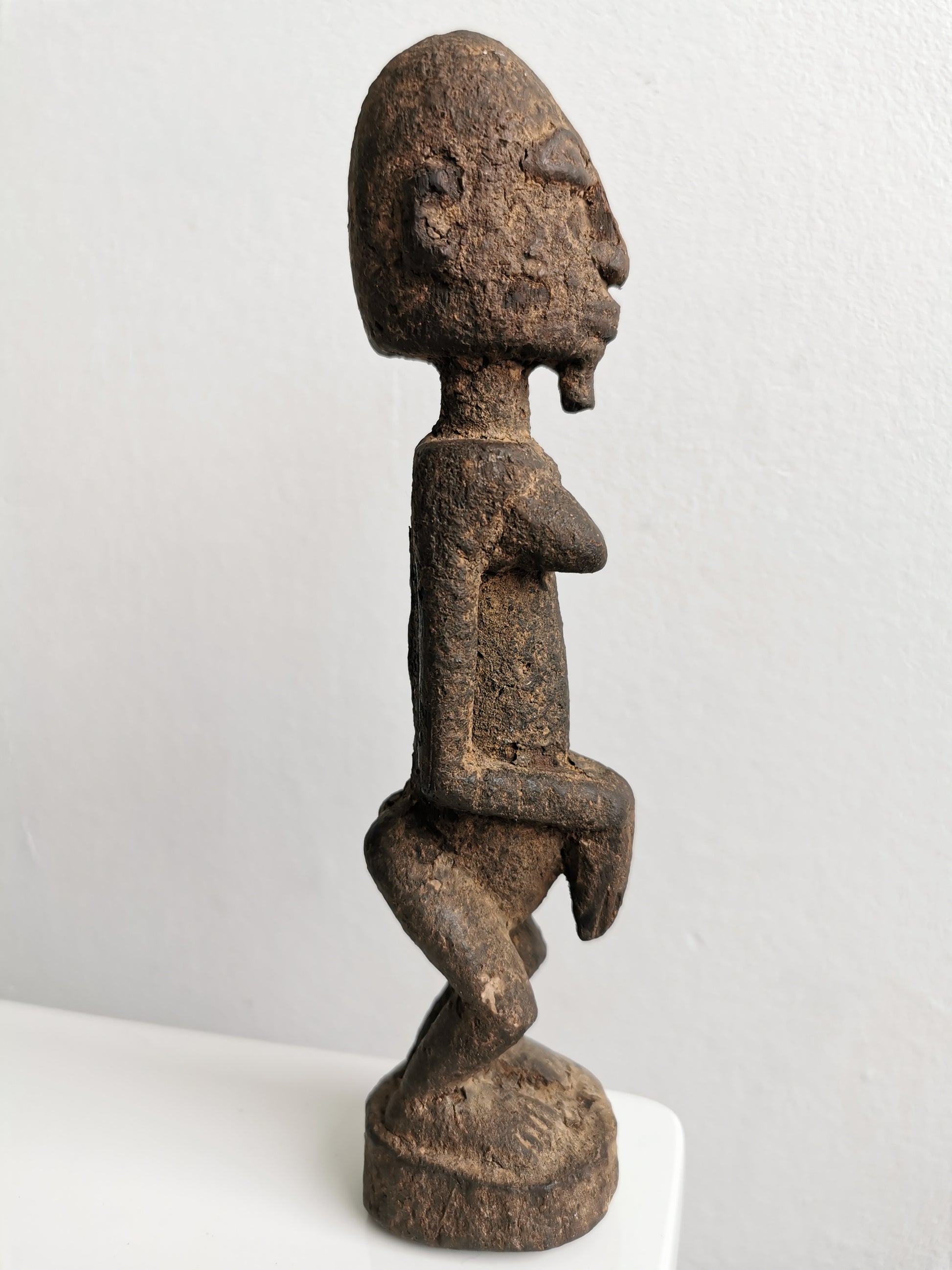 Profile view of the Lobi figure, showing its slender, elongated body and the subtle curve of its back