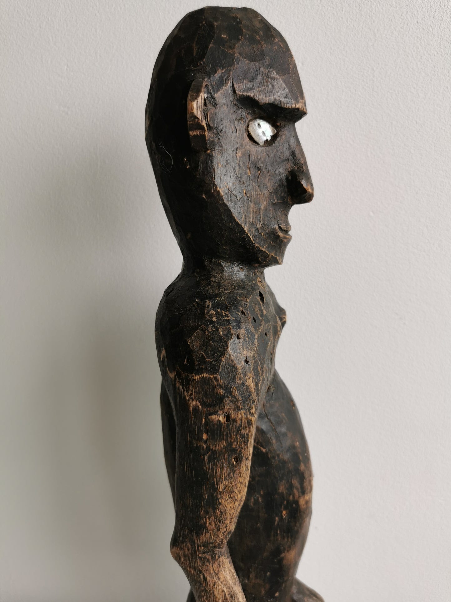 A side profile of the West African ancestor statue, showing its slender form and the carving of the limbs.