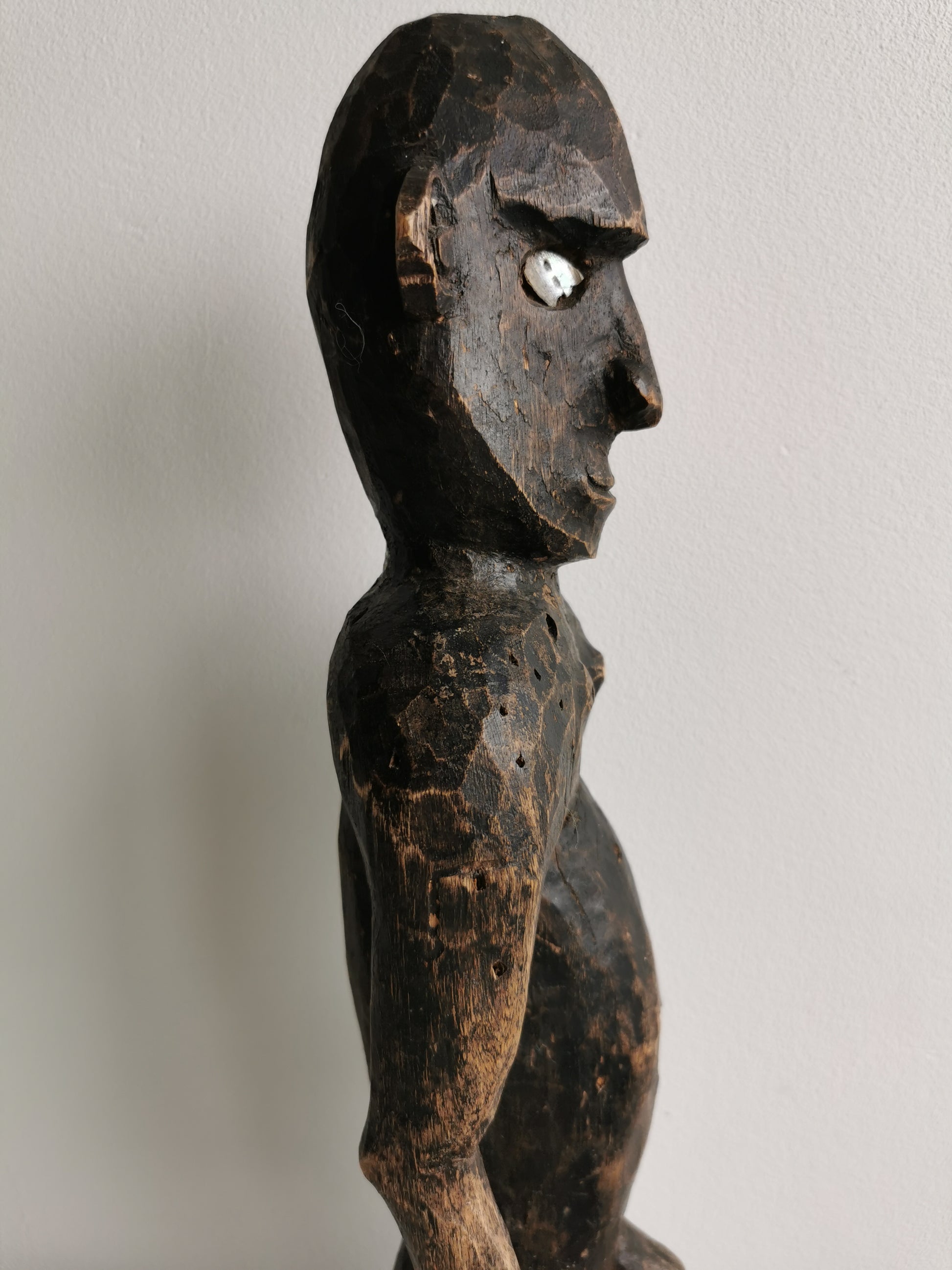 A side profile of the West African ancestor statue, showing its slender form and the carving of the limbs.