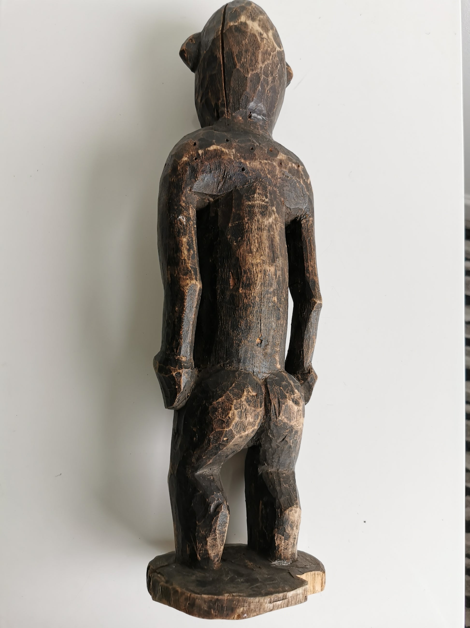 A back view of the wooden statue, revealing the details of its carved headdress and the natural texture of the wood grain.