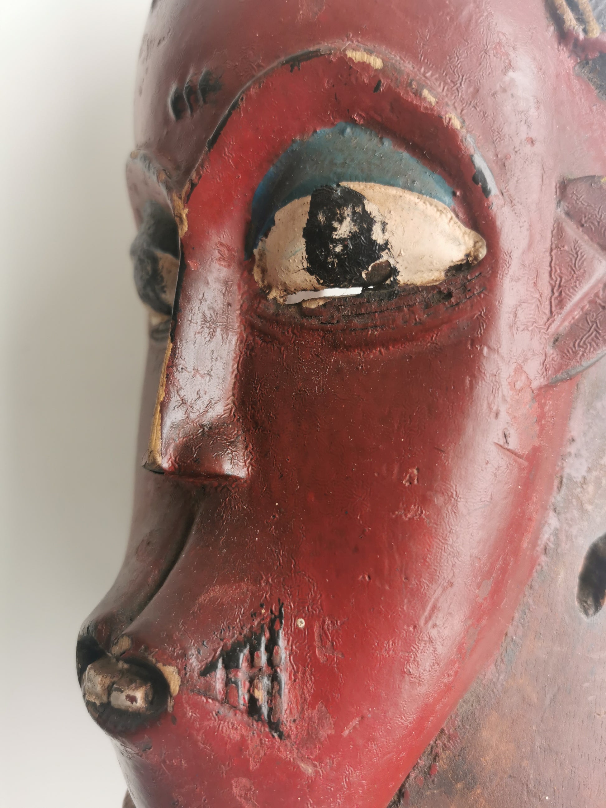 A close-up of the mask's face, highlighting the expressive, outlined eyes, the scarification marks on the cheeks, and the small, open mouth.