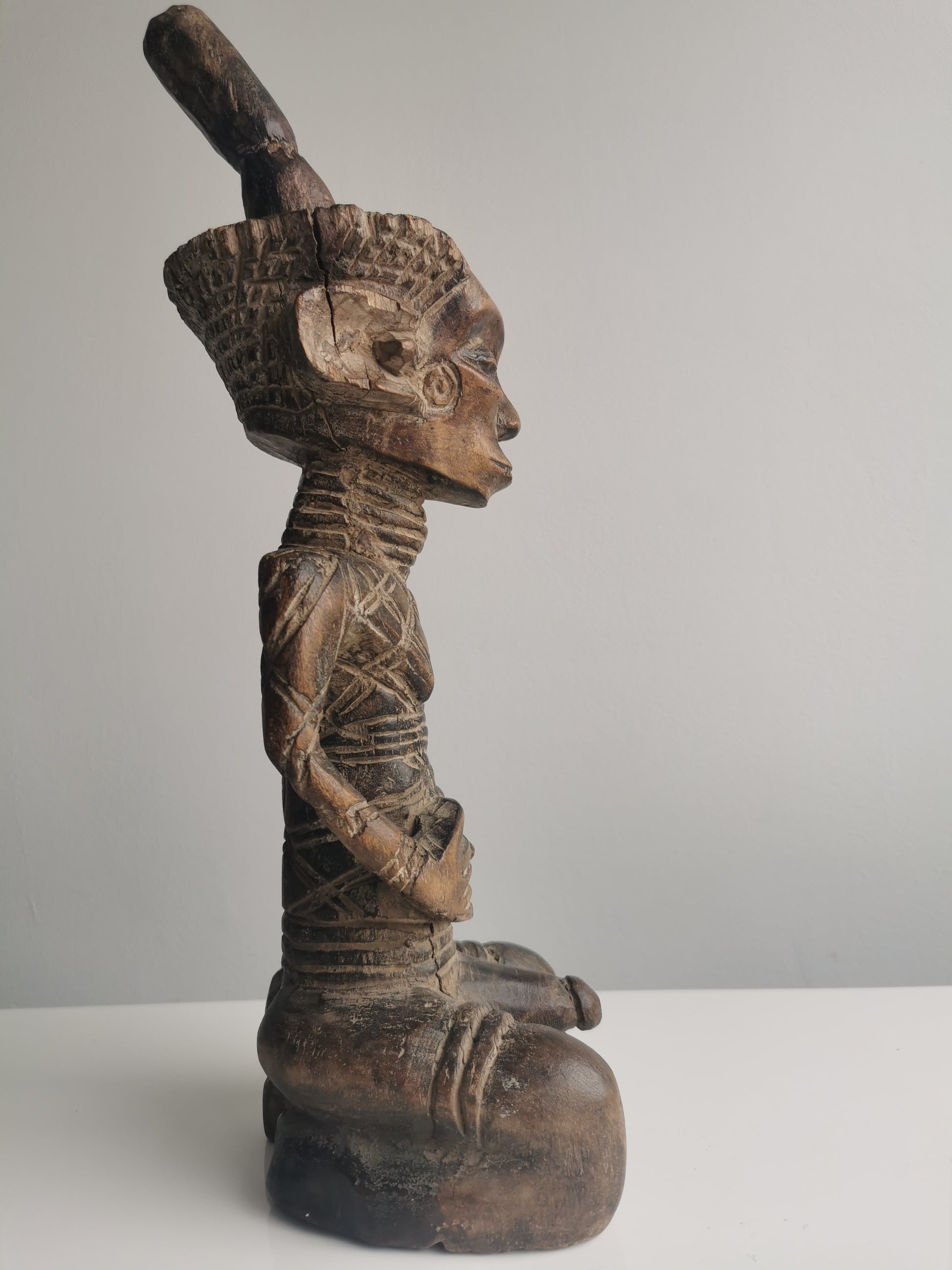 A side profile of the Dengese statue, showing the full seated figure and its prominent headdress.