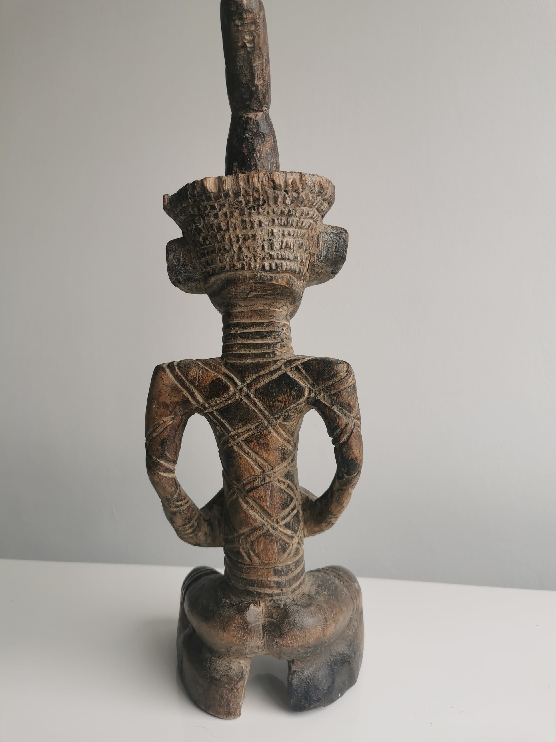 A back view of the wooden statue, revealing the details of the carving on the headdress, back, and buttocks.